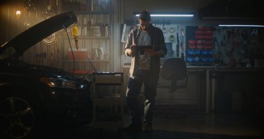 Açık Başlıklı Genç Adam, Tablet 'i Açık Kapüşonlu Araba' nın yanında duruyor ve Tanı Sonuçlarını Aktif İzliyor. Dizüstü bilgisayar Rolling Cart Connected Car 'a yakın bir yerde. Modern Teknik Ustalık, Dijital Analiz.