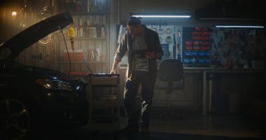 Açık Başlıklı Genç Adam, Tablet 'i Açık Kapüşonlu Araba' nın yanında duruyor ve Tanı Sonuçlarını Aktif İzliyor. Dizüstü bilgisayar Rolling Cart Connected Car 'a yakın bir yerde. Modern Teknik Ustalık, Dijital Analiz.