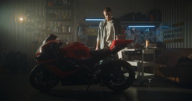 Sunlit Garajı 'nda Genç Adam Temizlik Spreyi Motosikleti Spreyliyor ve Yüzeyi Mikrofiber Bez ile Cilalayıp Güneş Işığı Altında Bisiklet Parıltılarının Tadını Çıkartıyor. Sahiplik Gururu ve Motosikletler İçin Tutku.