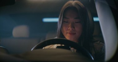 Asyalı Kadın, Nişanlı Telefon Konuşması sırasında Arabasını Garajdan Hazırlıyor. Kadın, hoparlörden konuşurken araba sensörlerini takip ediyor. Modern Şehrin Hızlı tempolu Yaşam Tarzı Konsepti.