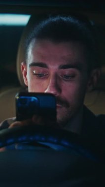 Saçları arkadan bağlanmış adam arabada oturur, akıllı telefondan mesajlar okur. Adam, Yanıt Yazmadan önce Düşünceli Duraklatır, Önemli, Anlamlı Konuşmaya Girer. Sosyal İletişim. Dikey Çekim.