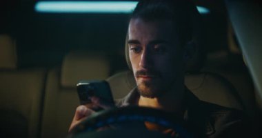 Saçları bukleli genç adam direksiyonun arkasında oturur, akıllı telefona odaklanır. Kararlı, Erkek Tipleri Uzun Mesaj Yazıyor, Dikkatlice Kelimeleri Seçiyor. Dijital İletişim Üzerine Duygusal İlişki.