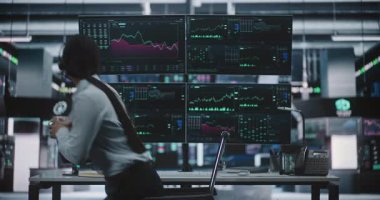 Kadın Tüccar, öğle yemeği molasından sonra elinde bir fincan kahveyle işe geri döndü ve Modern Borsa Merkezi 'nde yerini aldı. Dört Monitörle İş İstasyonunda Oturan Kadın Gerçek Zaman Çizelgeleri Gösteriyor.