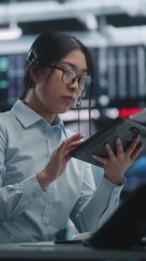 Asyalı Kadın Danışmanlık ve Tablet Kullanma, Dijital Çalışma İstasyonu. Kadın Finansal Uzman Yüksek Teknoloji Ofisi 'nden Küresel Varlıkları yönetiyor, Tablet ve Profesyonel Kulaklıkla Çoklu Görev Yapıyor. Dikey Çekim.