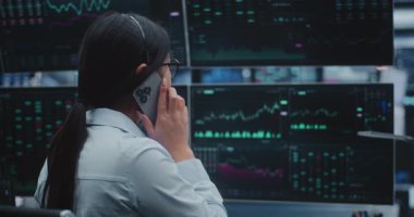 Dört Büyük Ekran Arasında Verileri İzlerken Akıllı Telefon 'da Piyasa Eğilimlerini Tartışan Kadın Borsacı. Massive Innovative Digital Hub 'da Gerçek Zamanlı Finansal Danışmanlık, Çoklu Görev.