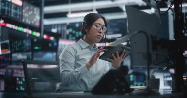 Tablet ve Çoklu İzleme Sistemi aracılığıyla odaklanmış Asyalı Kadın Ticareti Analiz Etme Eğilimleri. Gözlüklü Kadın Çalışma İstasyonunda Oturuyor, Dijital Tablet 'teki Gerçek Zaman Verilerini Çapraz Referans Ediyor ve Kulaklıkla Konuşuyor.