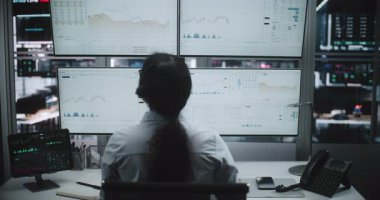 Kadın Simsar, Çoklu Ekran Analizlerini İzlerken Masa Telefonu Kullanıyor. Female Koordinates Market Operasyonu Gerçek Zamandaki Borsa Çizelgeleri ve Tablet Verilerini Gelecek Takas Merkezinde analiz ederken. Arka Görünüm.