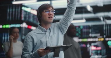 Gözlüklü ve Kulaklıklı Erkek Tüccar Apaçık İsyancı Ticaret 'e aktif olarak katılıyor. Tableti gerçek zamanlı analizlerle kullanan adam el işaretini yükseltiyor. Sayısal Çağ Açık İsyan Ticareti.