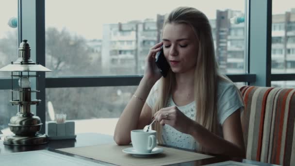Девушка разговаривает по телефону в кафе и пьет чай — стоковое видео
