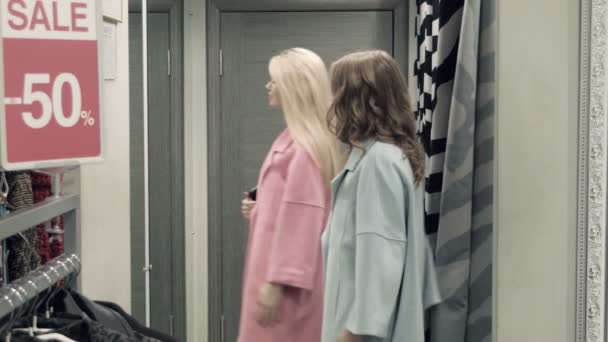 Zwei Mädchen probieren einen Mantel in einer Umkleidekabine an — Stockvideo