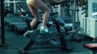 Atletik kadın simülatör spor sabit bir bisiklet üzerinde pedal.