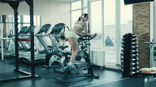 Sportliche Frau tritt im Fitnessstudio im Simulator auf einem stationären Fahrrad in die Pedale. — Stockvideo