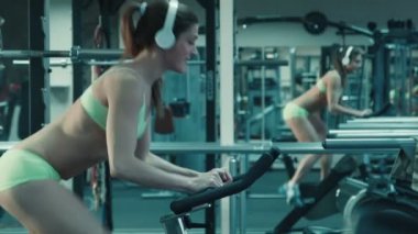 Simülatör spor sabit bir bisiklet üzerinde pedal kulaklık ile atletik kadın.