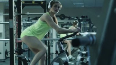 Simülatör spor sabit bir bisiklet üzerinde pedal kulaklık ile atletik kadın.