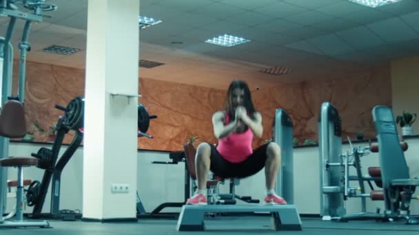 Jong meisje aan het doen squats en springt op fitness stap — Stockvideo