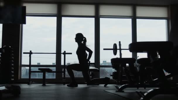 The silhouette of the young girl, does squats jumps in a gym — Stock Video