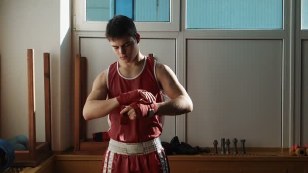 El joven boxeador tira del vendaje rojo en las manos y comienza a boxear — Vídeo de stock