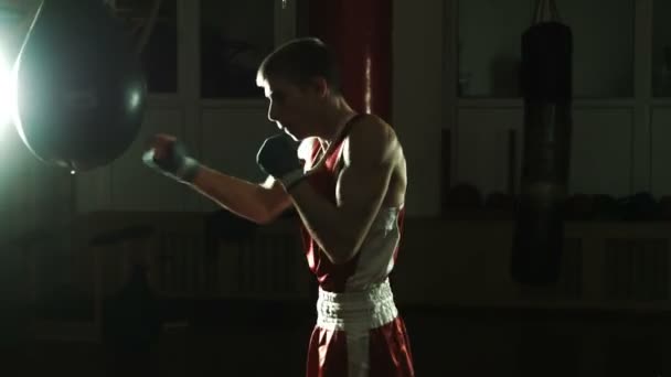 Силуэт молодого боксера, бьющего боксерскую грушу в тренажерном зале — стоковое видео