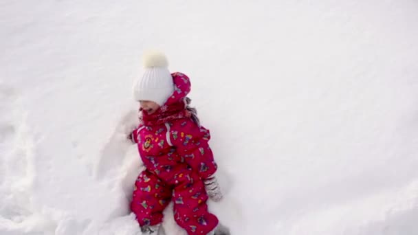 Маленькая девочка падает на снег и смеется — стоковое видео