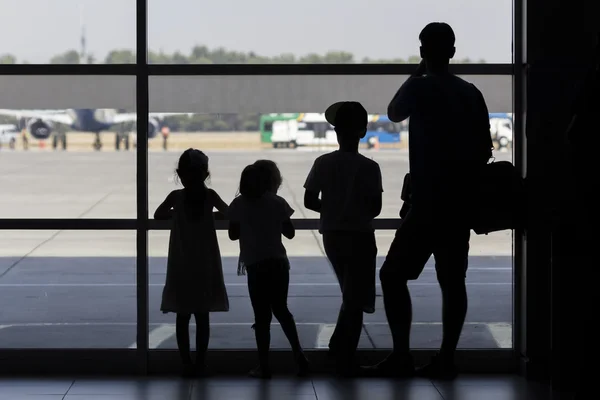 Silueta familiar frente a la ventana en el aeropuerto mirando aviones aterrizaje — Foto de Stock
