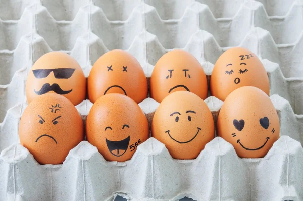 eight brown eggs  with faces drawn  arranged in carton
