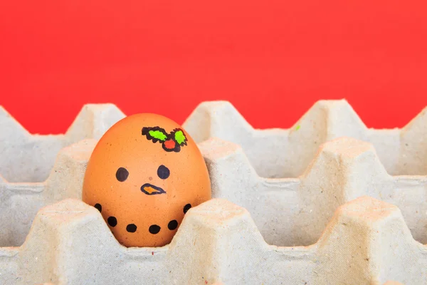 Vánoční vejce s tváře byly uspořádány v kartonu o červené backgro — Stock fotografie
