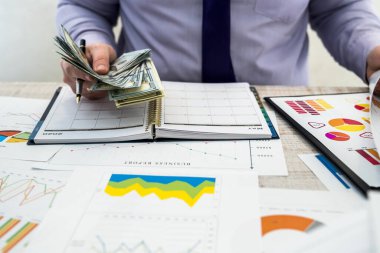 Ofiste çalışan bir iş adamı. Bir adam mal kiralamak ya da satmaktan kazanç elde ediyor. İş Analizi ve Strateji Konsepti. Masada dolar olan iş grafikleri ve belgeler.