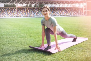 Yeşil çimlerin üzerinde paspas üzerinde esneme egzersizleri yapan bir kadın.
