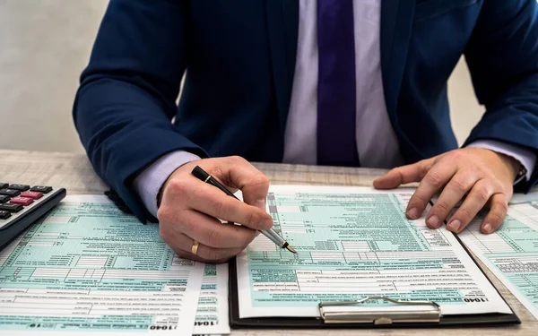 スーツを着た男が1040個の納税申告書を記入している 税金の時間だ 会計の概念 — ストック写真