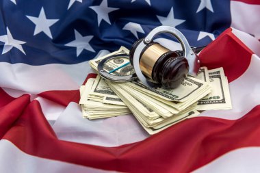 Metal kelepçeler, hakimin çekici ve Amerikan bayrağında duran dolar banknotları. Mali suçlar veya yolsuzluk kavramı