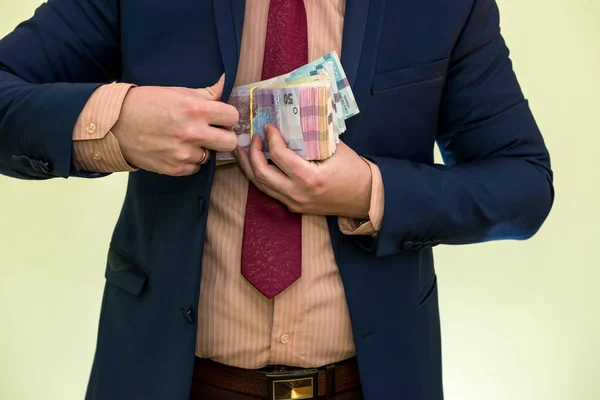 Business man hiding pack of Ukraine in suit pocket. The concept of corruption and fraud. UAH 1000 new hryvnia banknotes