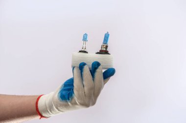Eldiven içinde insan eli, yeni halojen araba ampulleri tutuyor, izole edilmiş. Otomobil farları için lamba