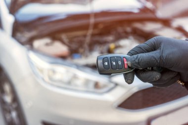 Otomotiv tamircisi arka planda araba ve kaputu açık halde anahtarları elinde tutuyor. Onarım