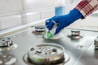 Mutfakta lastik eldivenlerle paslanmaz çelik gaz yüzeyi temizleyen kadın..