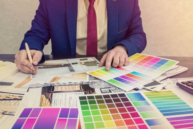 Genç tasarımcı modern bir apartman dairesi seçimi ve onarımı üzerinde çalışıyor. Ofisteki masada düz ve renkli desenler çiz