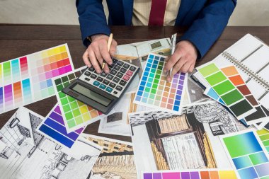 Genç tasarımcı modern bir apartman dairesi seçimi ve onarımı üzerinde çalışıyor. Ofisteki masada düz ve renkli desenler çiz