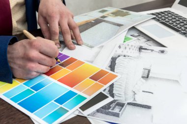 Mimarlar, yaratıcı masa ve ofis üzerinde renk örneği ve dizüstü bilgisayarla modern dairelerin çizimlerini yapıyorlar. Oda dekorasyonu için renk seçen adam