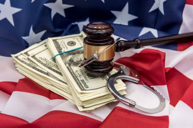 Metal kelepçeler, hakimin çekici ve Amerikan bayrağında duran dolar banknotları. Mali suçlar veya yolsuzluk kavramı