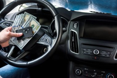 Adam otomobilde oturuyor ve ödeme ya da alım için para sayıyor. Dolar ve araba anahtarı.