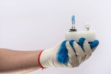 Eldiven içinde insan eli, yeni halojen araba ampulleri tutuyor, izole edilmiş. Otomobil farları için lamba