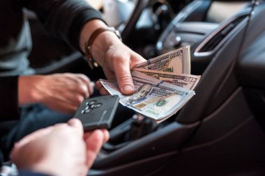 Adam otomobilde oturuyor ve ödeme ya da alım için para sayıyor. Dolar ve araba anahtarı.