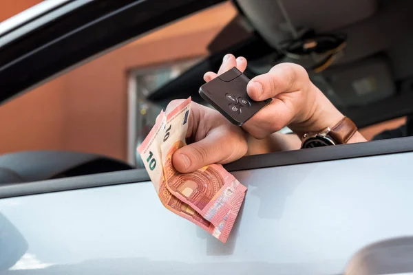 male\'s hand holding euro bills and key inside car for buy or rent. finance