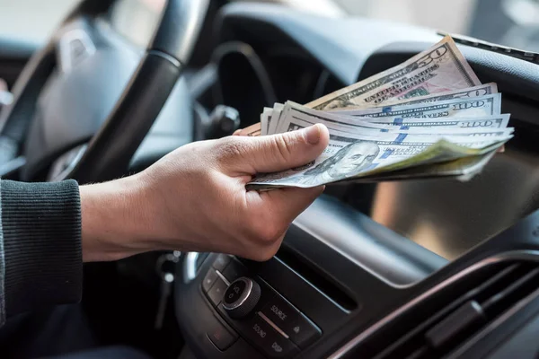 businessman pays for a product or service, gives dollars while sitting in the car. finance concept