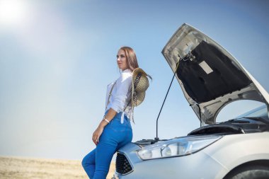 Bozuk arabanın motoruna bakan güzel genç bir kadın. Yolculuk sorunları.
