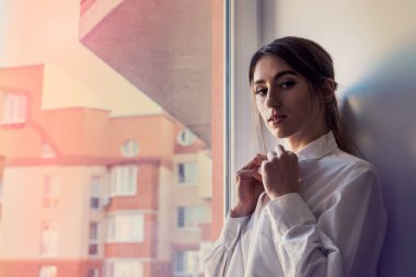 Pencere kenarında poz veren güzel kız, güneşin tadını çıkarıyor.