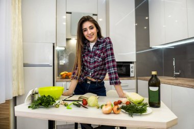 Genç bir kadın mutfakta not defterini kullanarak yemek pişiriyor. .