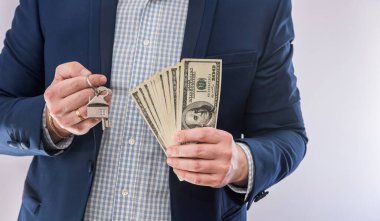 Amerikan dolarlarını tutan erkek eller ve evin anahtarı izole edilmiş. Konsept satın alma veya emlak kredisi 