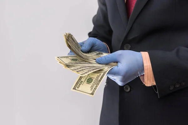 Man in suit holding money dollars 100 bills in medical gloves  for safety.  Coronavirus crisis. covid-19