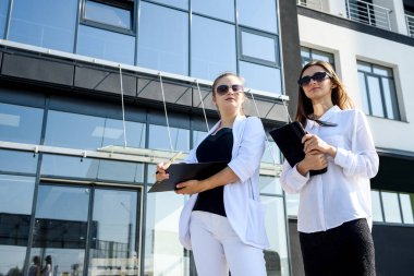 İş arkadaşları ellerinde tablet ve panoyla büyük ofis merkezinin önünde duruyorlar.