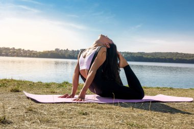 Güzel genç bir kadın sabah parkta çalışmadan önce esneme egzersizi yapıyor.